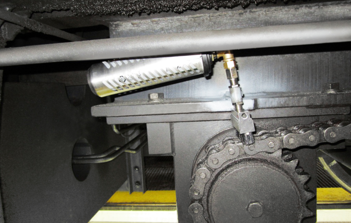 Le graisseur simalube 250ml lubrifie la chaîne d'entraînement d'une grue de chantier sur rails. Le distributeur est en outre protégé par un capot de protection.